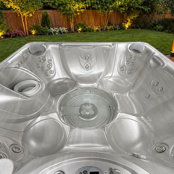 Empty silver hot tub with multiple jets in a backyard.