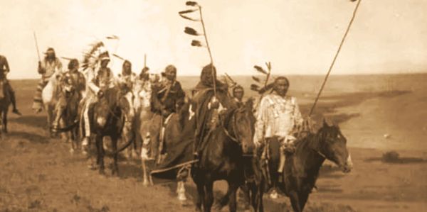 Historical photo of Native American horse riders in traditional attire.