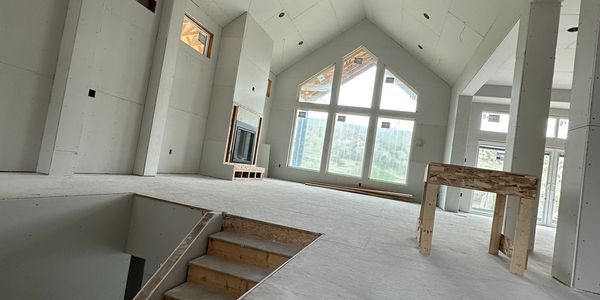 Unfinished house interior with large windows and staircase under construction.