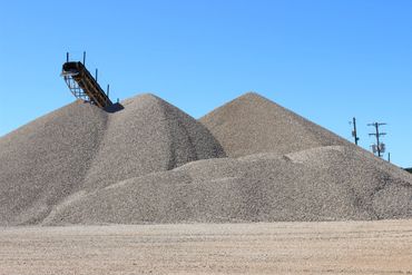 Large gravel piles with a conveyor belt under a clear blue sky.