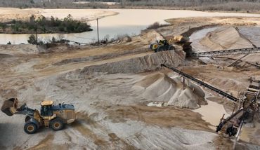 Construction vehicles at work in a sandy excavation site with water nearby.