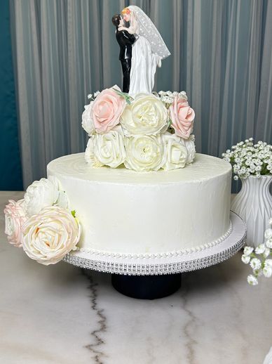 Elegant white wedding cake with floral decorations and bride-groom topper.