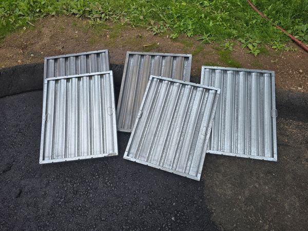 Five metal grates placed on the ground near grass and soil.