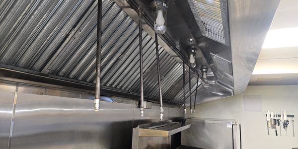 Industrial kitchen exhaust hood with hanging nozzles above cooking area.