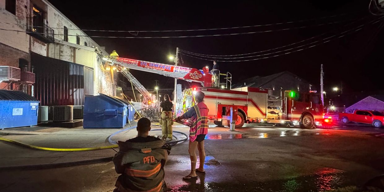 Firefighters respond to a nighttime fire at a building with a ladder truck and hoses.