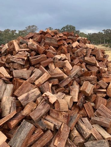 A large pile of chopped firewood outdoors under a cloudy sky.