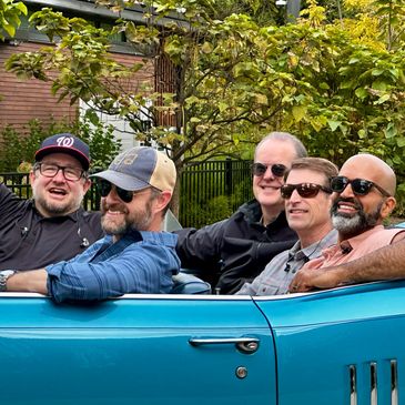 Five men smiling in a blue convertible car.