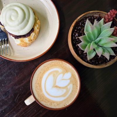 freshly baked cinnamon roll with a latte in a mug with latte art