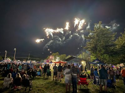 Crowd watching fireworks at an outdoor night festival with food stalls.
