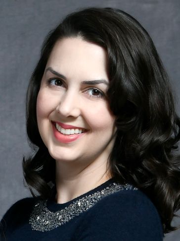Smiling woman with dark curly hair and a navy blue top with embellishments.