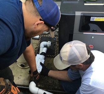 Two men working on plumbing with white PVC pipes.