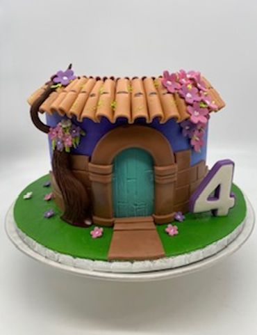A colorful house-shaped cake with a number 4 beside it on a green base.
