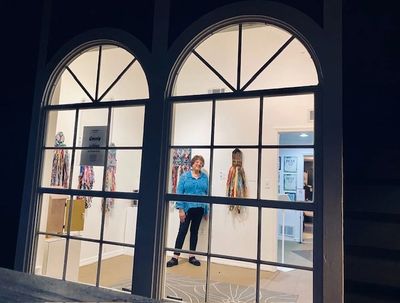 Person standing in an art gallery behind large windows at night.