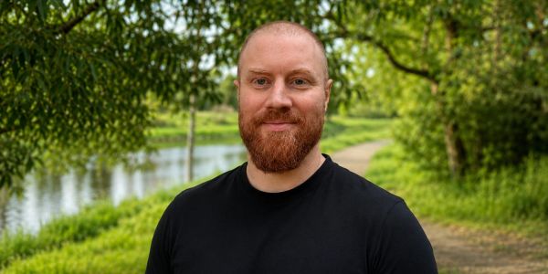 Man with a beard smiling outdoors.