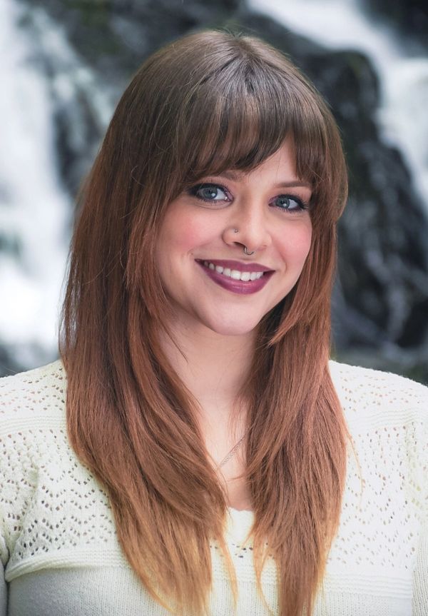 Smiling woman with long brown hair and septum piercing outdoors.