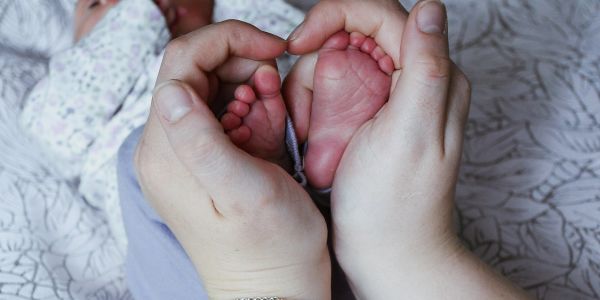 Hands gently holding a newborn's tiny feet in a heart shape.