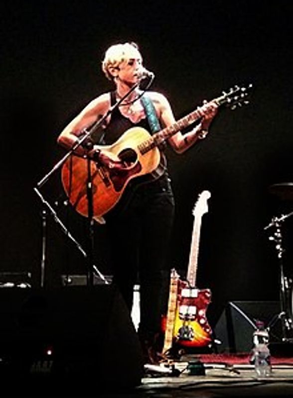 Musician playing acoustic guitar on stage under spotlight.