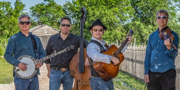 A four-member band playing banjo, double bass, guitar, and violin outdoors.