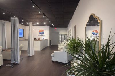 Modern, clean medical or wellness reception area with white furniture and plants.