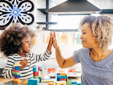 Mother and daughter giving a high-five while playing with colorful blocks.