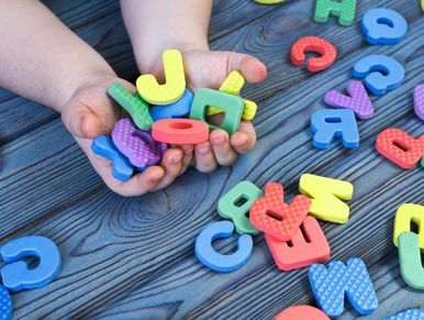 Child holding colorful foam alphabet letters on a wooden table.