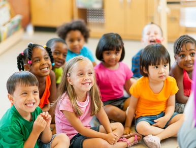 A group of diverse young children sitting on the floor, smiling and engaged.