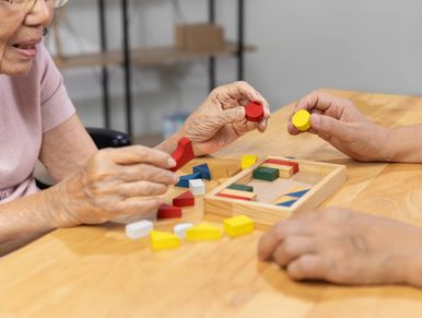 Elderly individuals playing with colorful wooden blocks at a table.