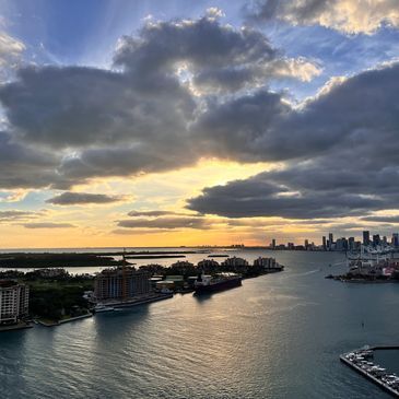 Sunset over a harbor with city skyline and dramatic clouds.