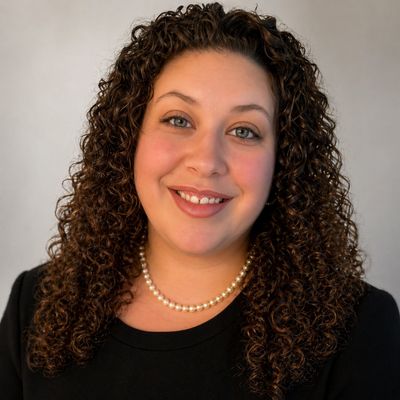 Smiling woman with curly hair wearing a pearl necklace and black top.