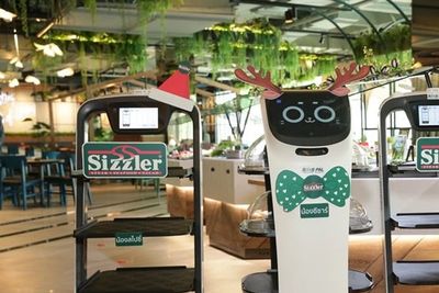 Cat-like delivery robot wearing reindeer antlers between two delivery robots wearing Santa hats