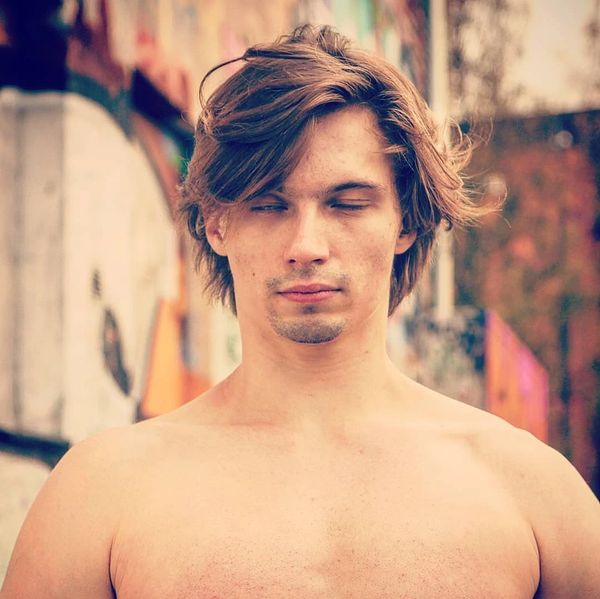 Young shirtless man with eyes closed in an urban setting.