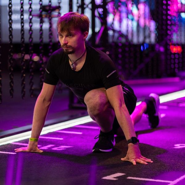 Man in workout gear stretching on gym floor under purple lighting.