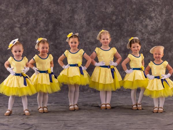Six young girls in yellow ballet costumes posing for a photo.
