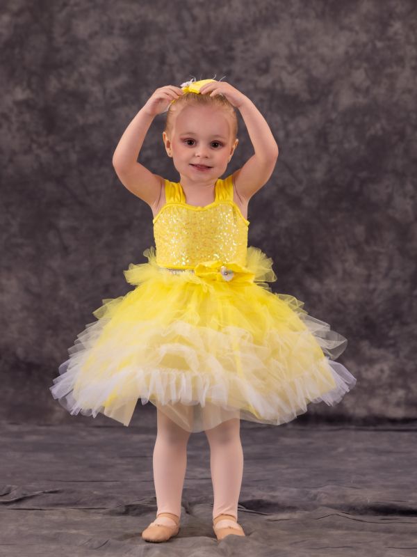 Young girl in a yellow ballet dress posing with arms above her head.