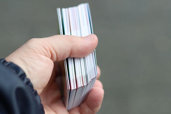 A close-up shot shows a person's hand holding a thick stack of trading cards.
