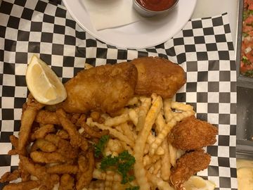 Cod shrimp and clams  and French Fries on a plate with a dipping sauce