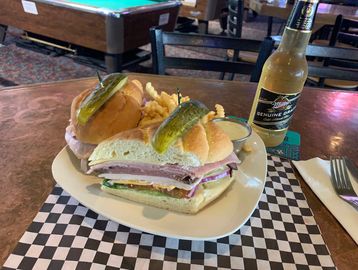 A huge deli sandwich  and French Fries on a plate with a dipping sauce and a beer