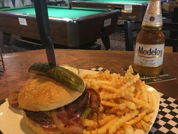 Bacon cheeseburger on a plate with french fries and a Modelo beer