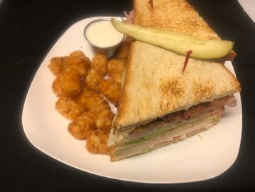 A huge club sandwich  and Tater Tots on a plate with a dipping sauce