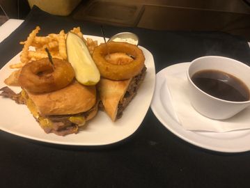 An 8 oz. top sirloin sandwich  and French Fries on a plate with a dipping sauce