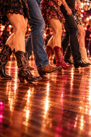 People line dancing in cowboy boots on a shiny wooden floor.