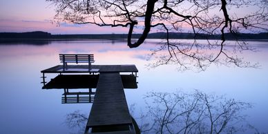Silhouette park bench, on jetty, reflection of tree in lake, sunrise, sunset, purple hues, lonely