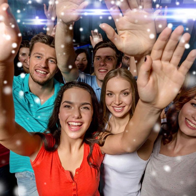 Group of friends smiling and waving at a party with festive lights.