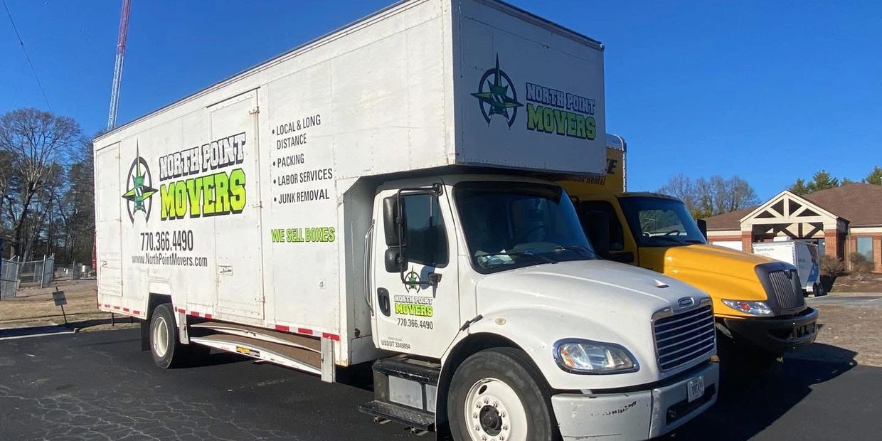 White moving truck with North Point Movers branding parked beside a yellow truck business relocation.