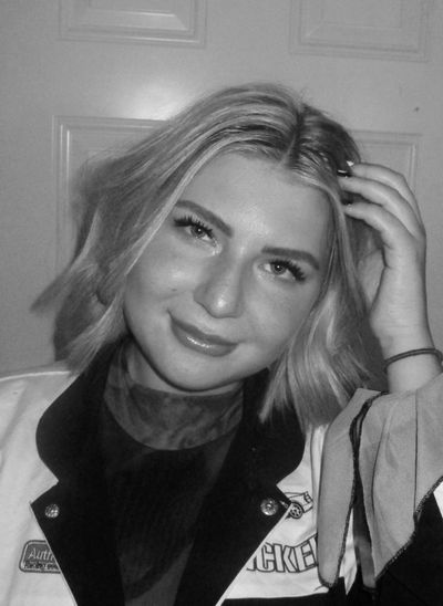 Young woman with blonde hair smiling, touching her hair.