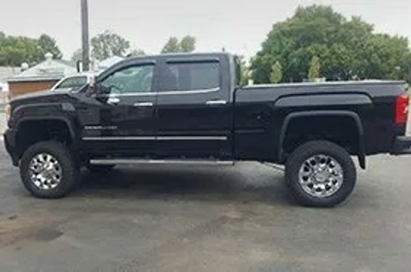 A black, lifted pickup truck with chrome wheels is parked outdoors on wet pavement.