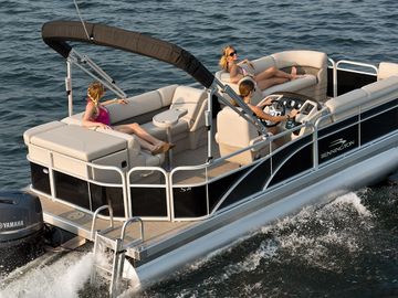 Three people relaxing on a pontoon boat cruising on water.