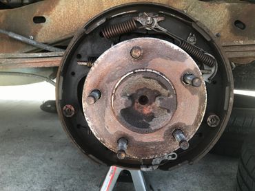 Rusty car drum brake assembly with visible springs and hub.