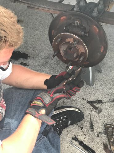 Person repairing a car brake system with tools and gloves.