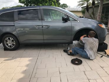 Person repairing a car tire in a driveway.